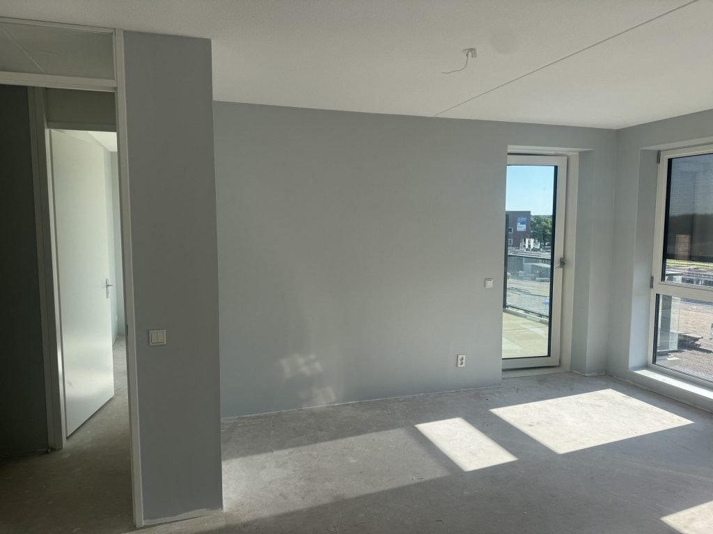 Nieuw appartement met lichtgrijs gesausde wanden, betonvloer en balkondeur