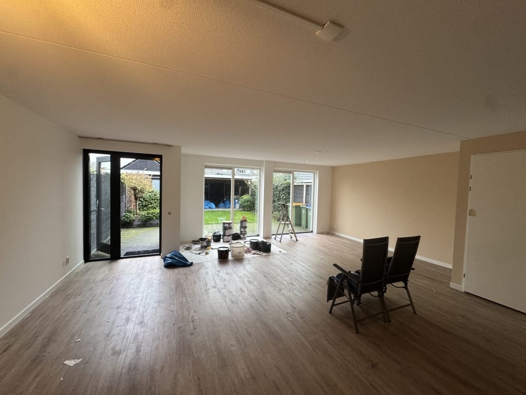 Lege woonkamer van een bestaande woning met verfemmers op de vloer en tuindeuren